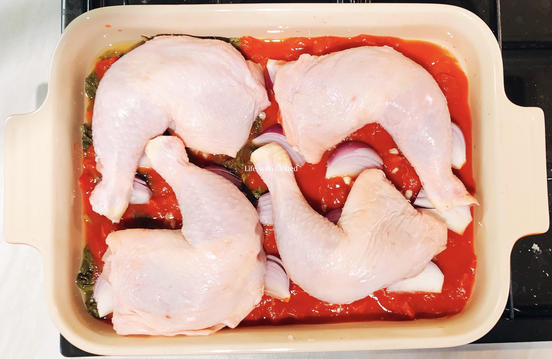 Raw chicken in oven dish on top of tomatoes and onions