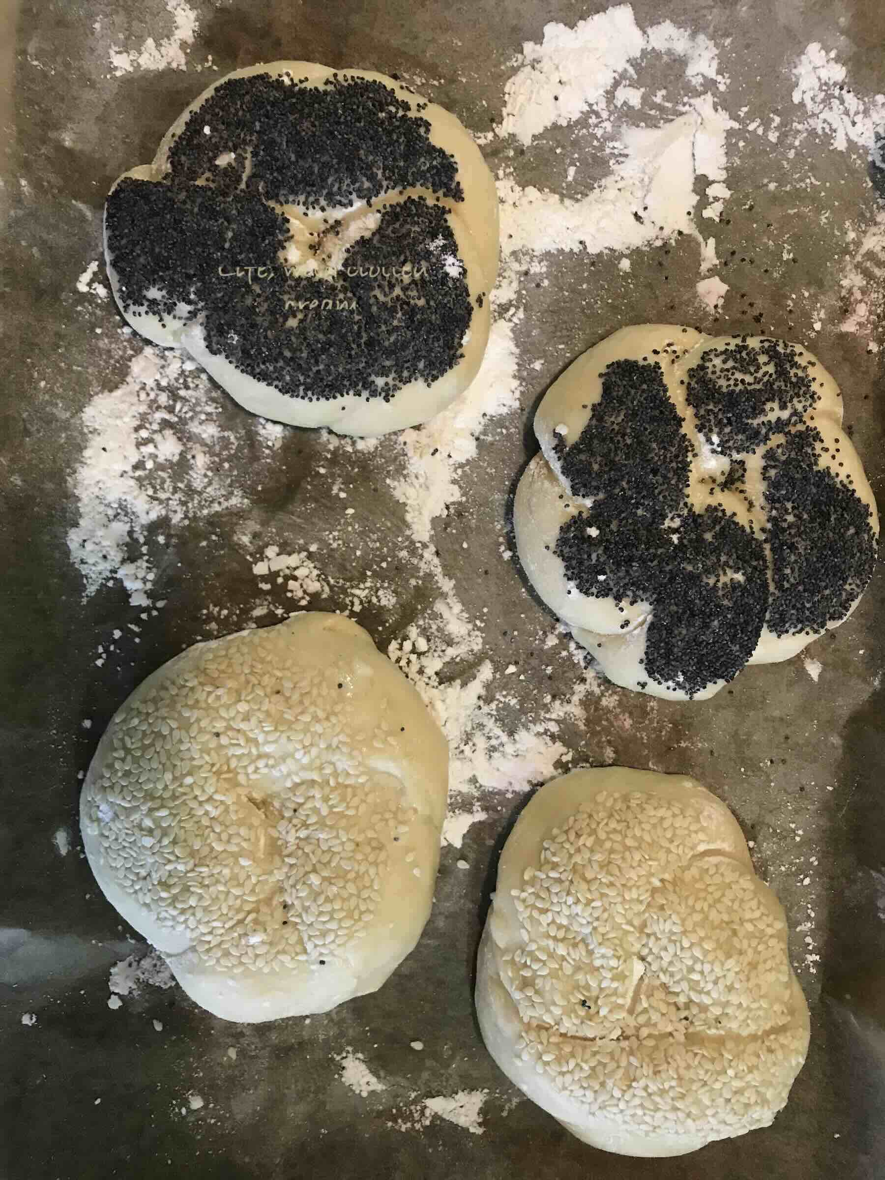Knotted kaiser rolls before they are baked on a baking tray in the oven, covered in white and black poppy seeds.