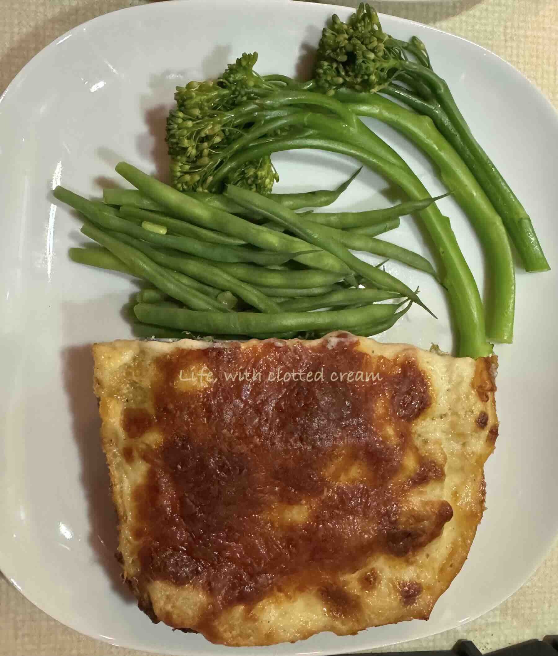 White chicken lasagna with golden crust and tenderstem broccoli and green beans on a white plate.