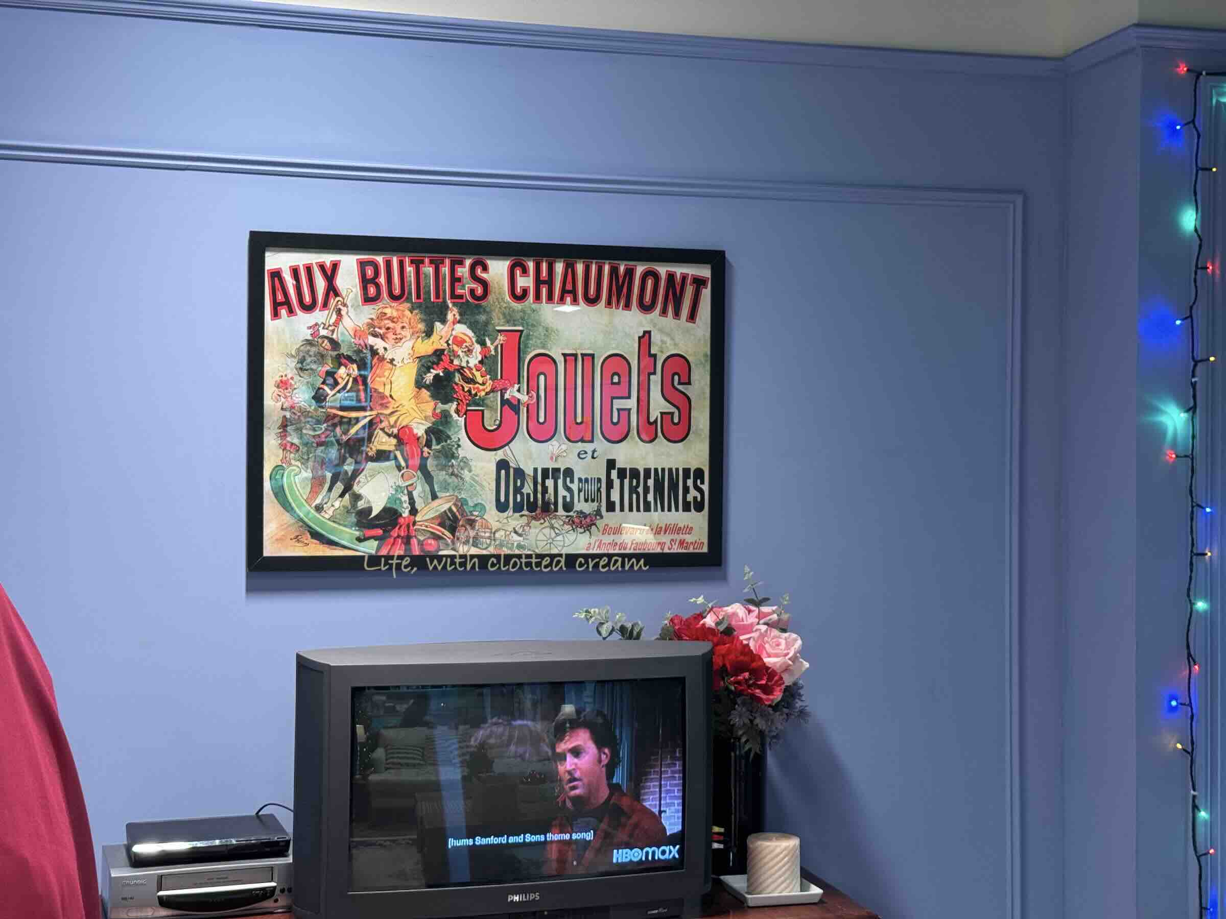 A french poster on a wall above a tv showing Friends