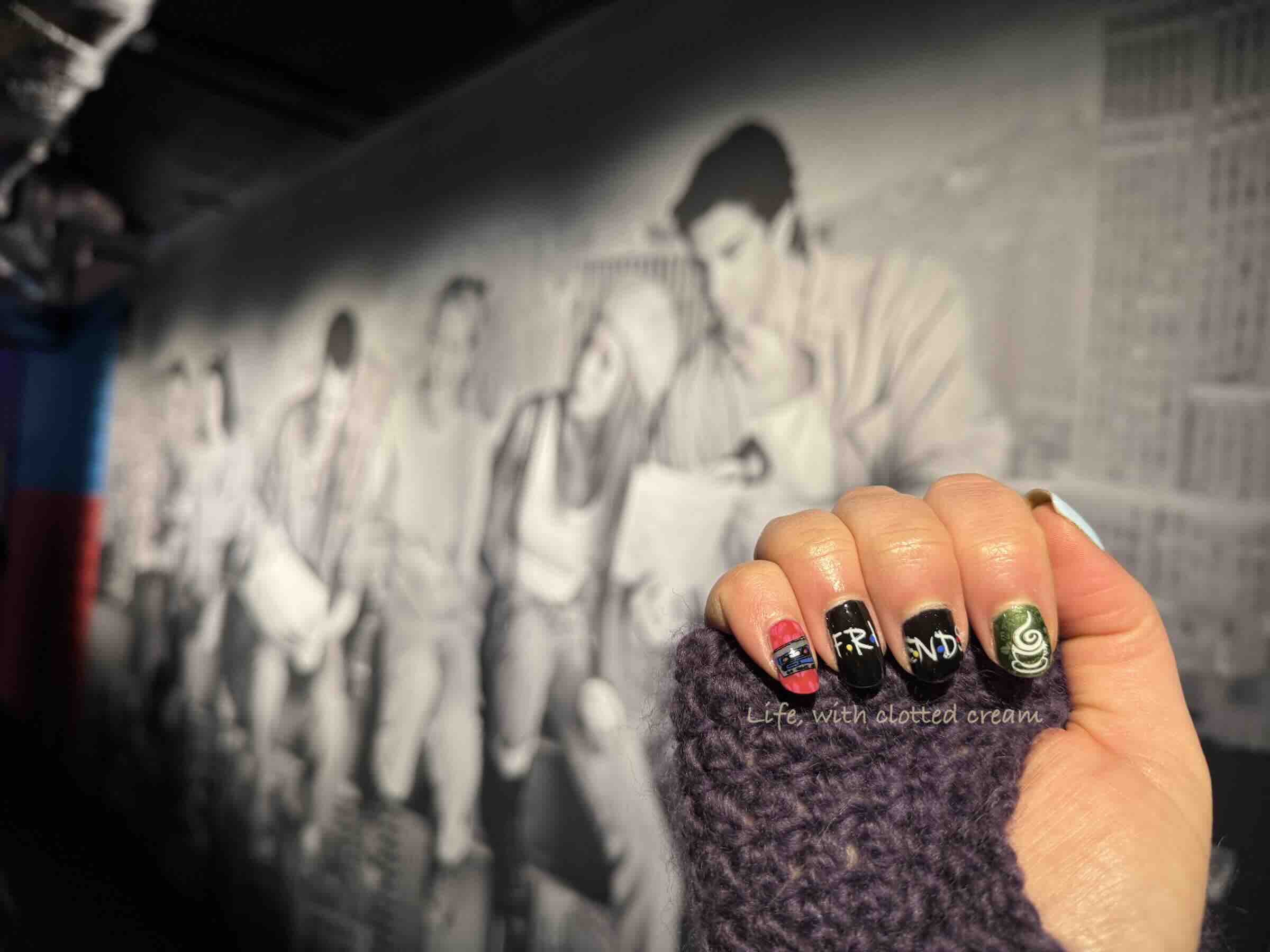 Black and white poster of the Friends cast in the background with a set of nails in the foreground painted with scenes from Friends.