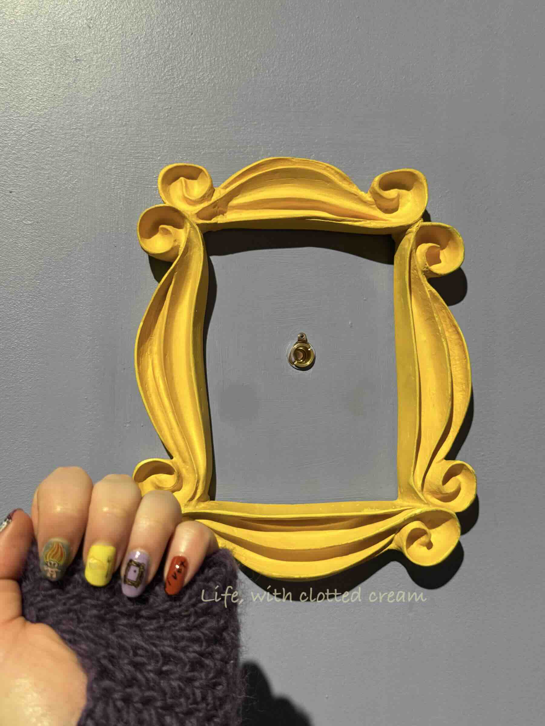 A purple door with a golden frame around a peephole with a set of Friends painted nails in front.
