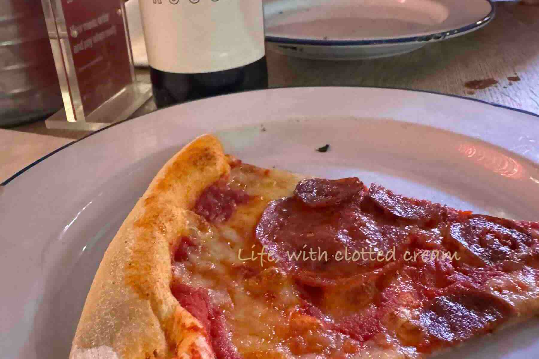 A white plate with a blue trim containing one slice of pepperoni pizza at Gordon Ramsay's Street Pizza in Battersea, London.