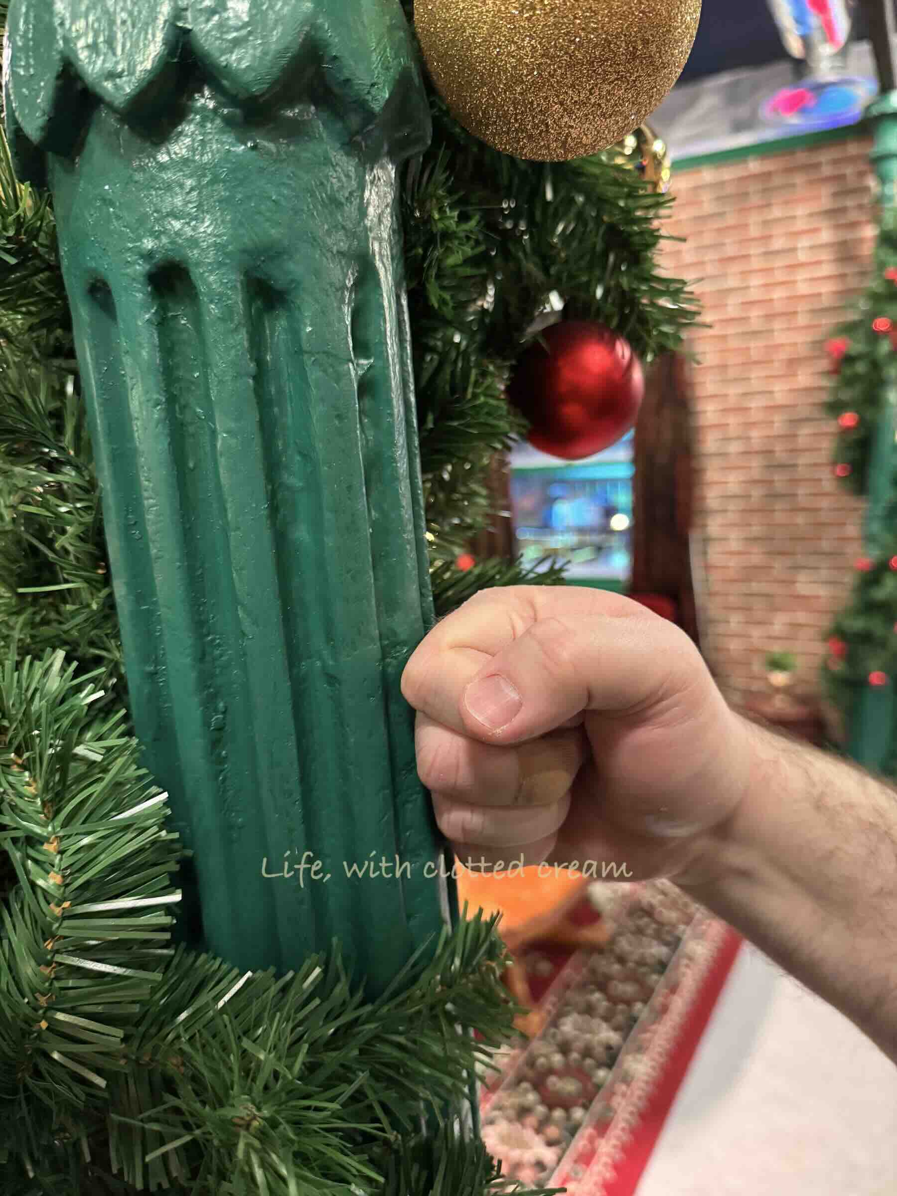 A green pillar in Central Perk with tinsel wrapped around it and a fist pretending to punch into it.