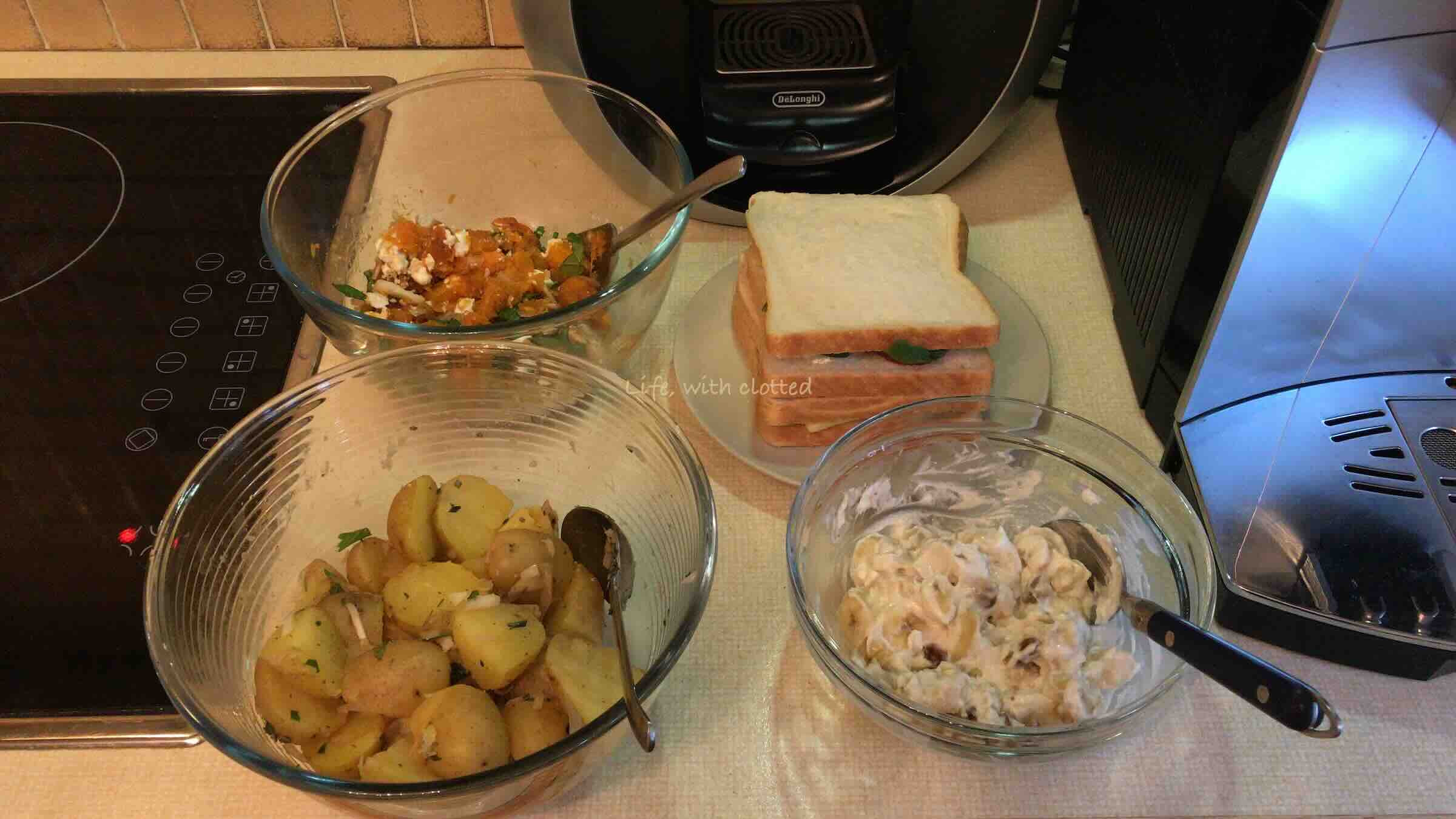 Two sandwiches and three salads with two coffee makers in the background.