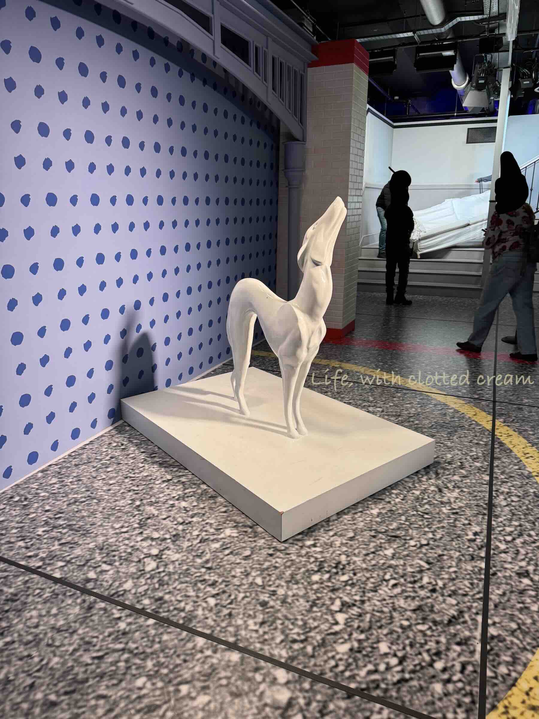 Pat the dog in the foreground and a white sofa halfway up a set of stairs at the Friends experience in London.