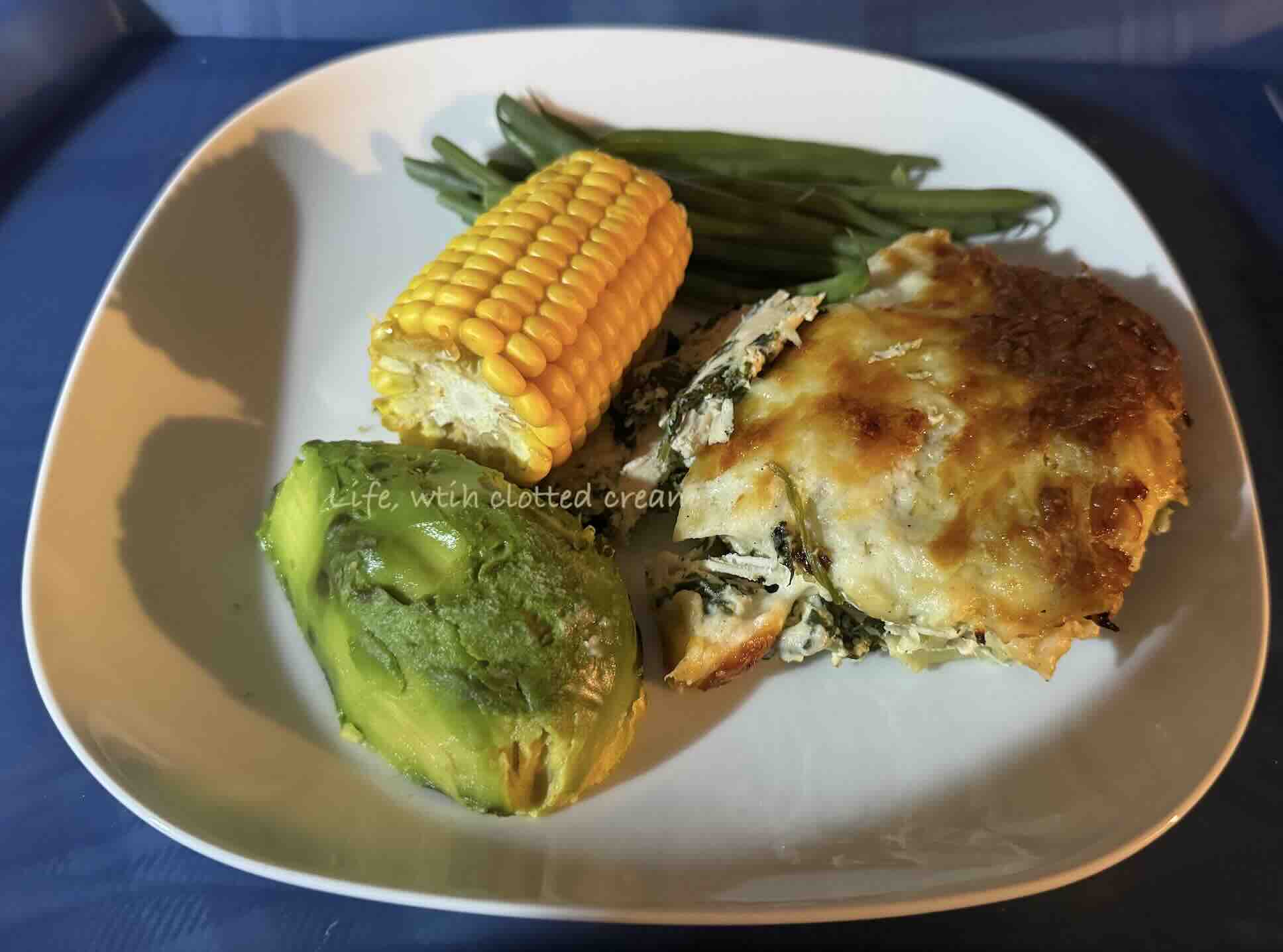 White chicken lasagna with golden crust and sweetcorn, avocado and green beans on a white plate.