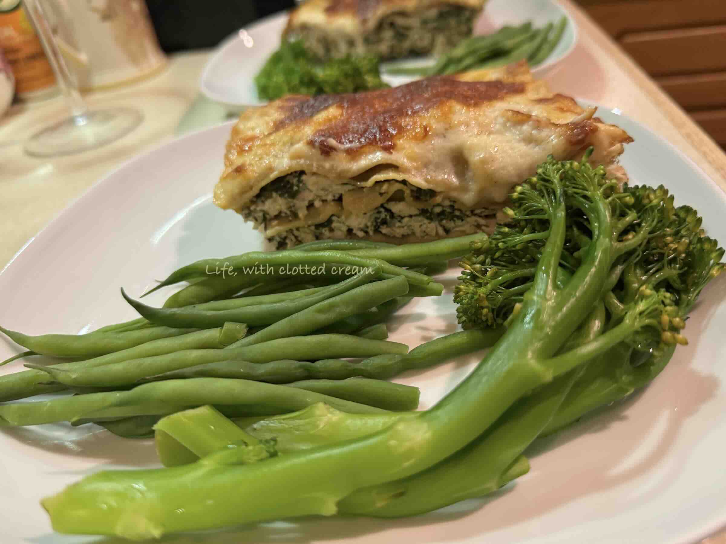 White chicken lasagna with golden crust and tenderstem broccoli and green beans on a white plate.