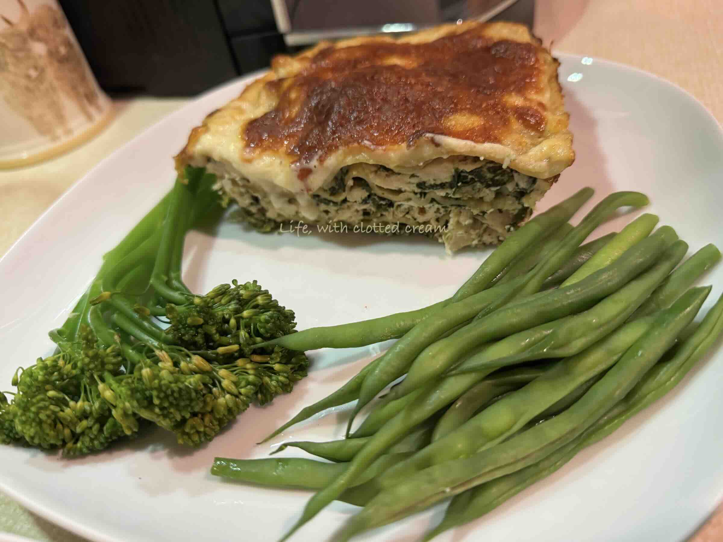 White chicken lasagna with golden crust and tenderstem broccoli and green beans on a white plate.