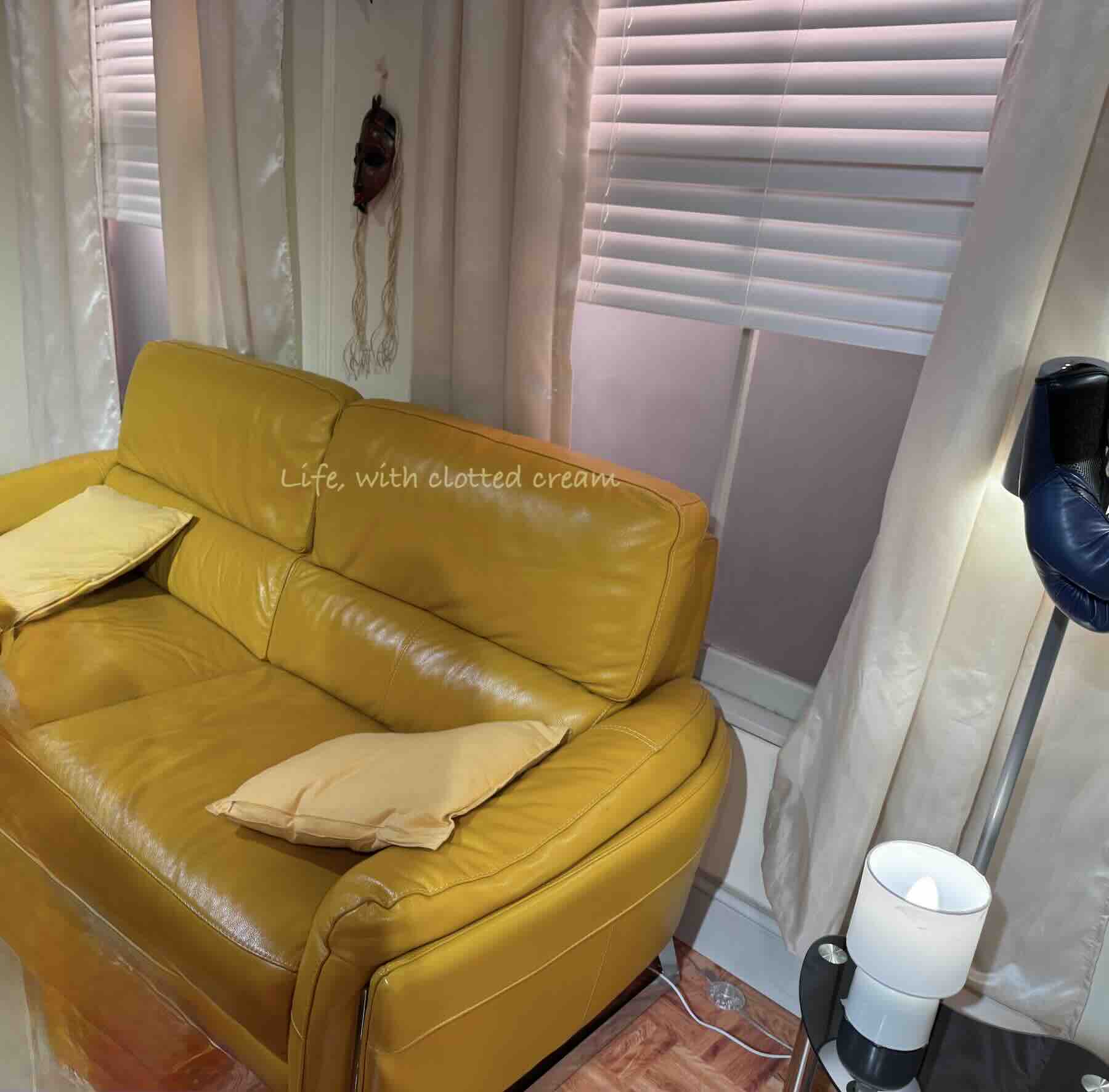 The yellow sofa in front of a window with blinds in Joey and Chandler's apartment.