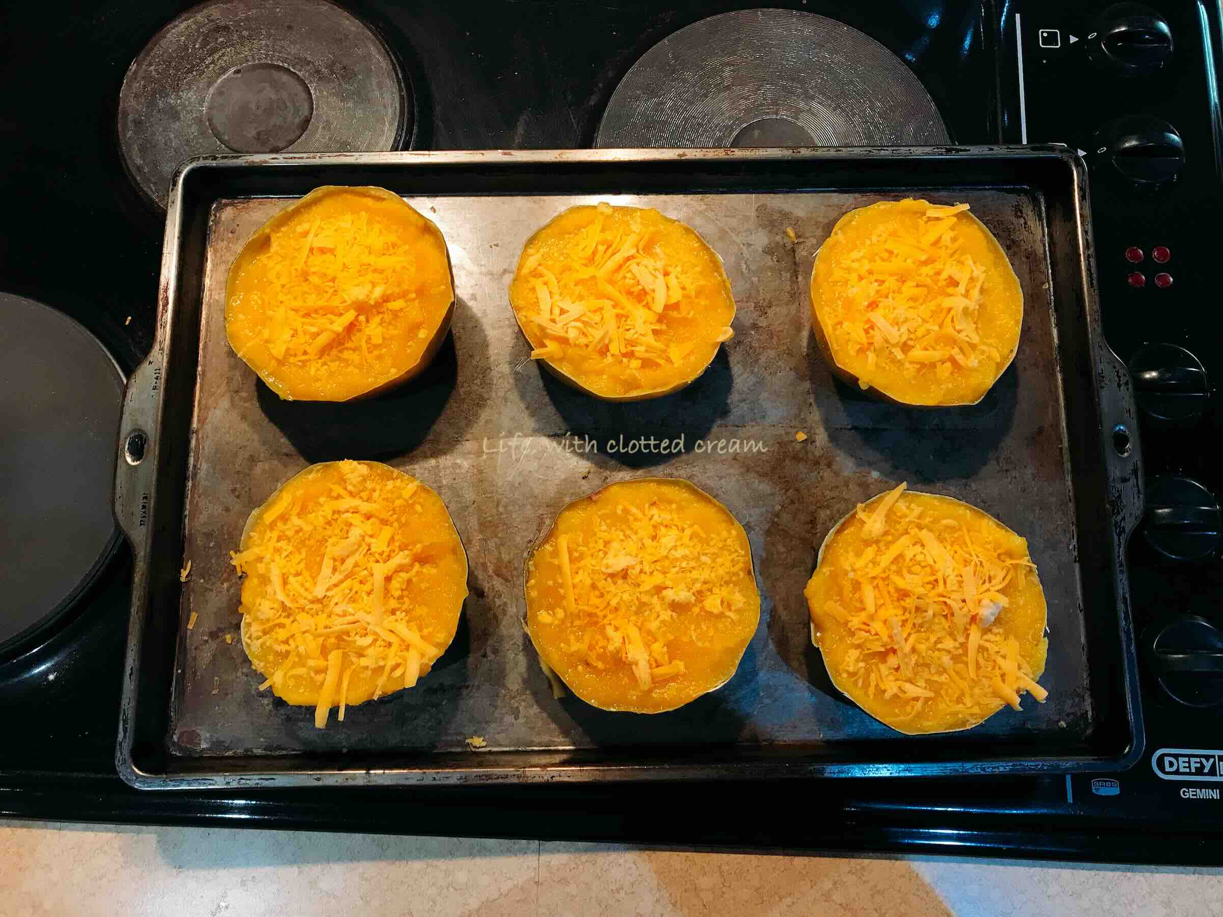 Filled gem squash topped with cheese on a seasoned baking tray.
