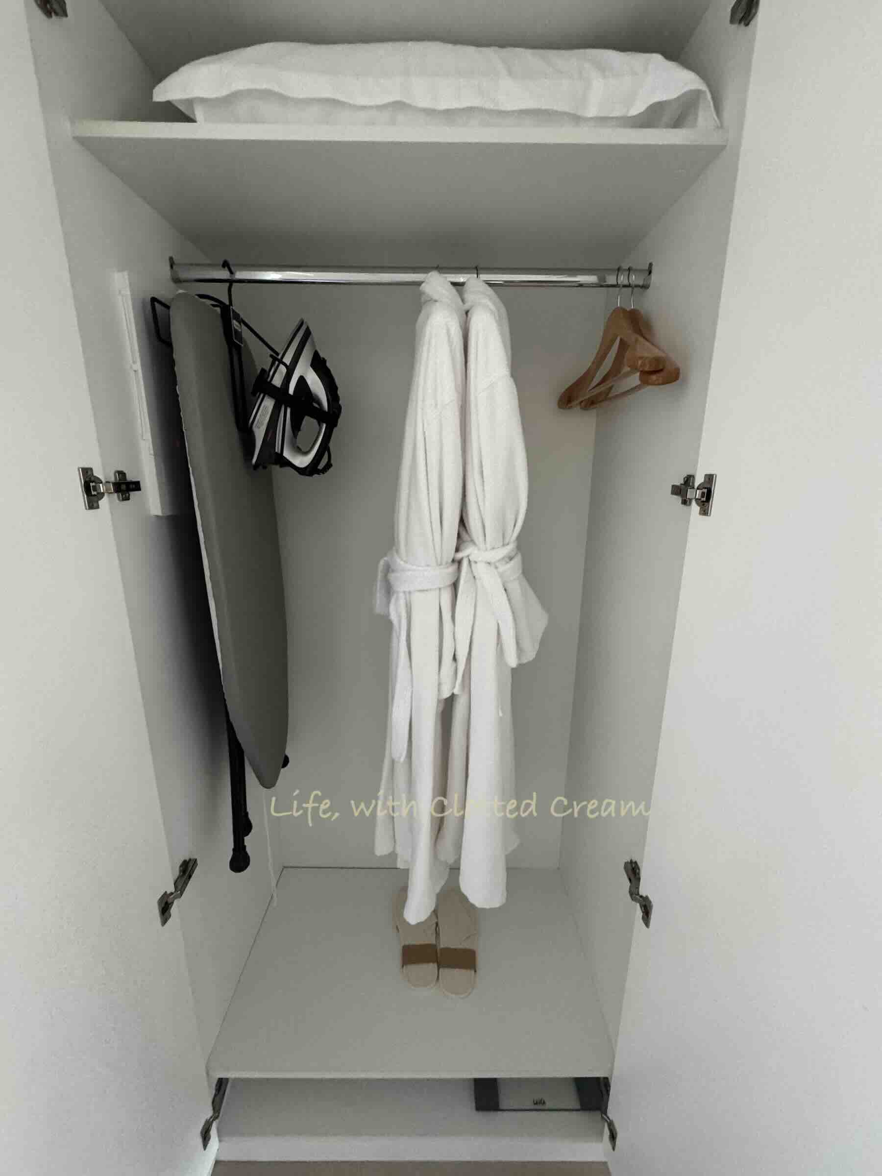 Ironing board with iron, bathrobes and hangers in a wardrobe.