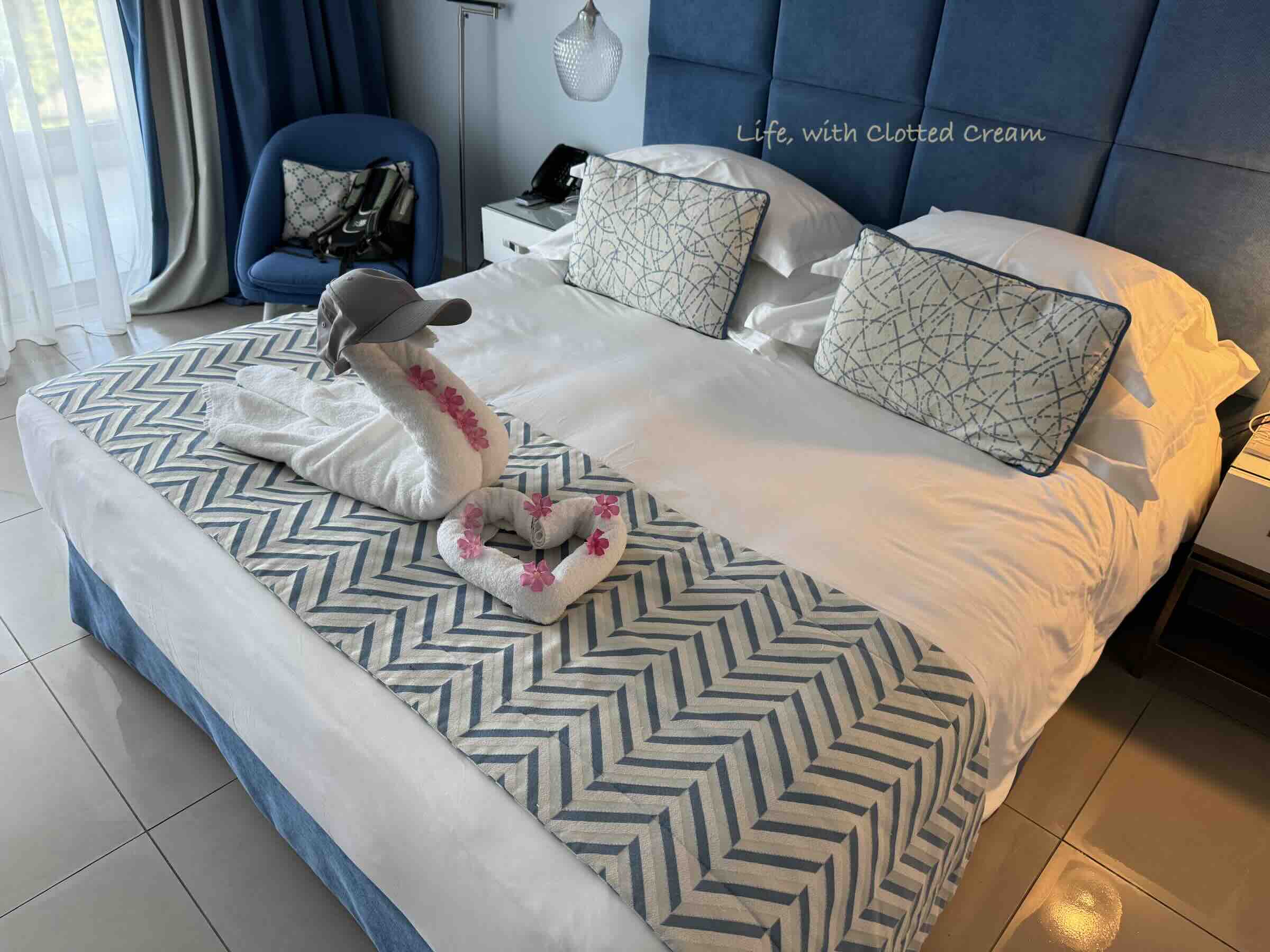 Double bed with towels arranged like a swan and pink flowers arranged around.