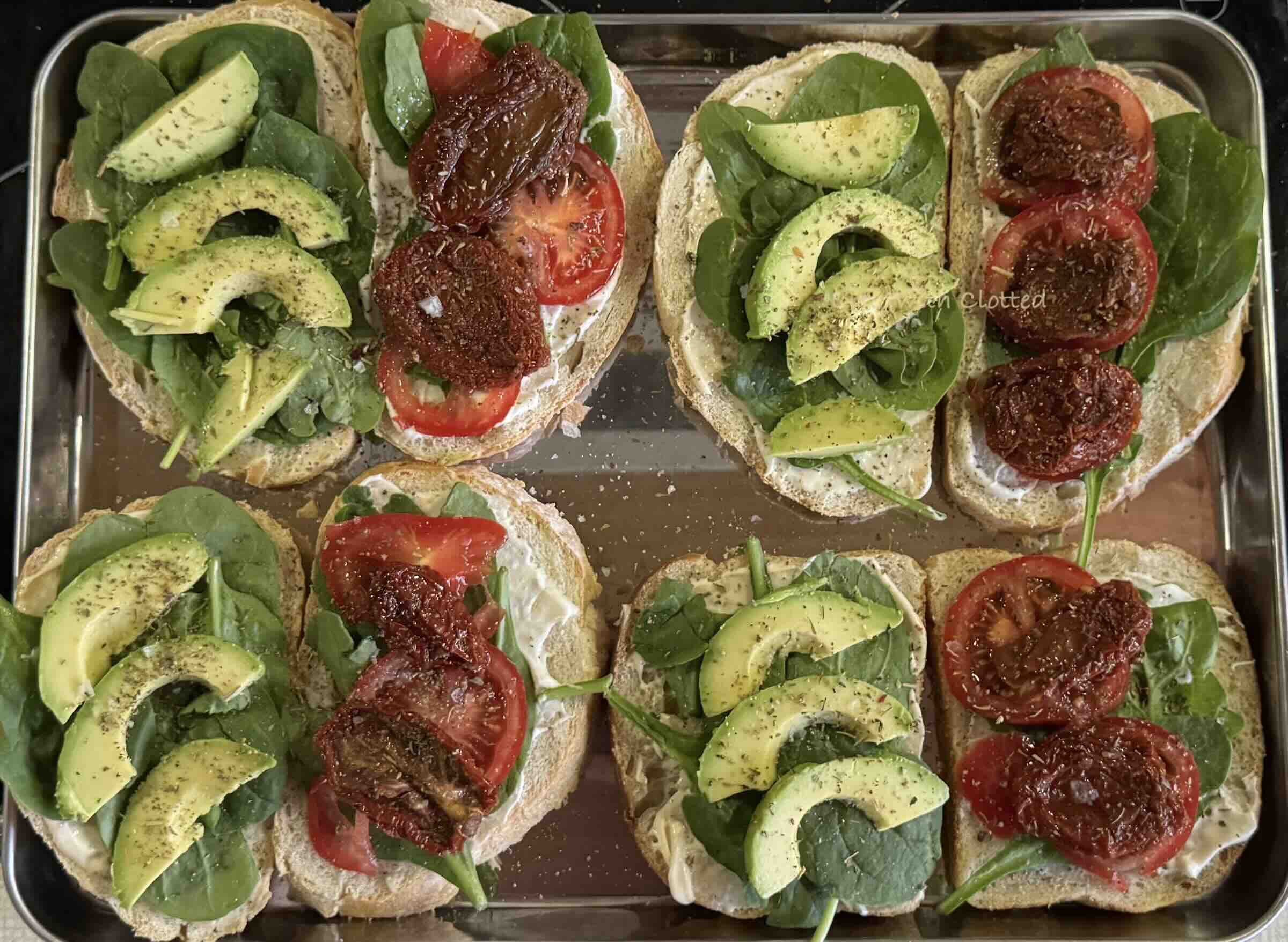 Bread with avocado on one side and slices of fresh tomatoes and sundried tomatoes on the other side.