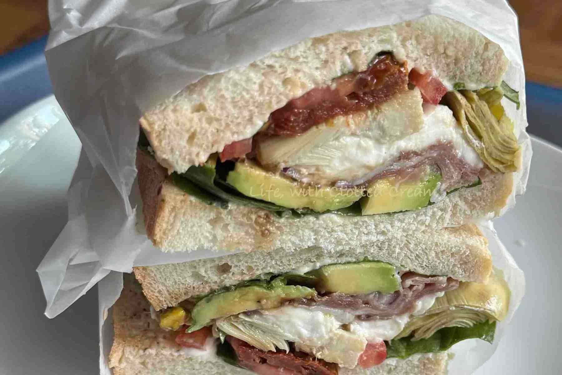 Mediterranean sandwich wrapped in greaseproof paper. It is cut in half to show off the layers.