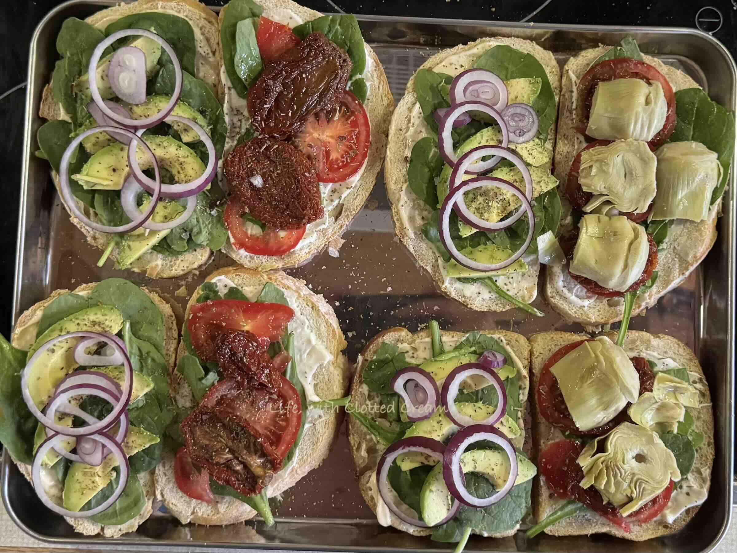 Slices of bread with red onion on one side and the other side has either fresh and sundried tomatoes or artichokes.