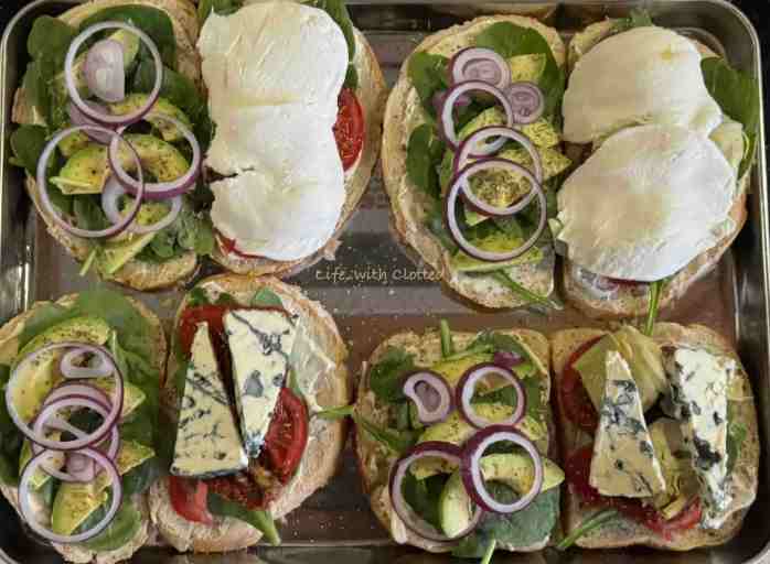Slices of bread covered in spinach, red onion and avocado on one side and mozzarella and blue cheese on the other.